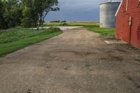 a dirt road going toward two barns in rural country setting with storm clouds overhead above