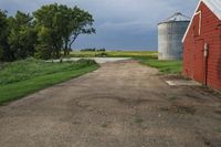 a dirt road going toward two barns in rural country setting with storm clouds overhead above