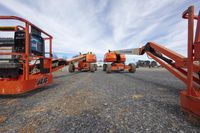 two hydraulic hand trucks parked on top of a gravel field in rural landscape and trees