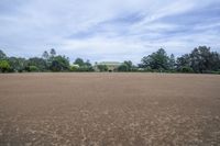 a field with lots of dirt and a large house in the distance there are trees in the foreground