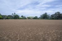 a field with lots of dirt and a large house in the distance there are trees in the foreground