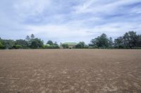 a field with lots of dirt and a large house in the distance there are trees in the foreground