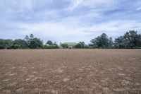 a field with lots of dirt and a large house in the distance there are trees in the foreground