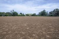 a field with lots of dirt and a large house in the distance there are trees in the foreground