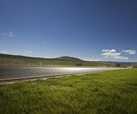 an empty highway in the middle of a pasture in a rural area under a blue sky