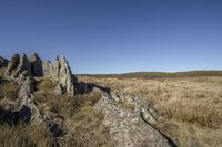 rock formations of rocks, standing in the grass and on the ground, in front of a clear blue sky