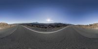 an empty desert road in the middle of nowhere and a mountain range in the background