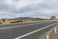 there is an empty road with a field and mountains in the background and a sign posted on a gate