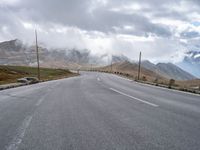 an empty road leads uphill towards mountains under cloudy skies over the horizon are power lines