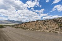 a dirt road stretches out into a mountain range on a sunny day, with blue skies