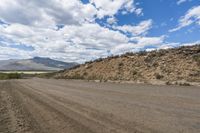 a dirt road stretches out into a mountain range on a sunny day, with blue skies