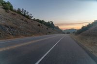 the road is next to some hills at sunset with a small tree line on the right side