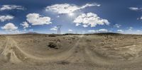 a panorama view of the sun shining over an empty field of dirt and grass with a telephone tower in the background