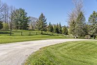 an empty country road winding through a field with a wooden fence and a dog gate