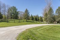 an empty country road winding through a field with a wooden fence and a dog gate