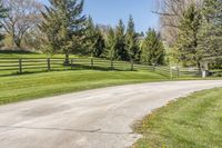 an empty country road winding through a field with a wooden fence and a dog gate