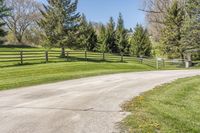 an empty country road winding through a field with a wooden fence and a dog gate