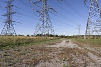 electricity towers with dirt roads and grass in a field on the outskirts of the town