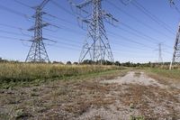 electricity towers with dirt roads and grass in a field on the outskirts of the town