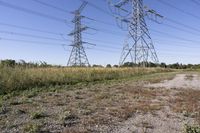 electricity towers with dirt roads and grass in a field on the outskirts of the town