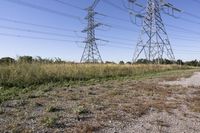 electricity towers with dirt roads and grass in a field on the outskirts of the town