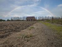 a house is in the middle of a field, with a rainbow in the background