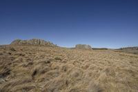 large rocks and brown grass in open grassy terrain with blue sky in the background and an orange cloud in the distance