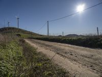 dirt road with fence and wind generators behind it during daytime in the desert with sun