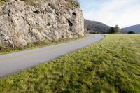 a scenic view of an empty street running along the cliff side of a large boulder face