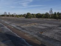 a empty parking lot with a few trees behind it and water running on the pavement
