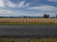 a empty road next to a field with a mountain behind it on a bright, cloudy day