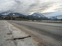 an open asphalt road leads to a body of water with snow capped mountains behind it