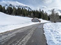 a road that runs to a cabin in the snow with mountains in the background behind