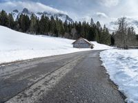 a road that runs to a cabin in the snow with mountains in the background behind