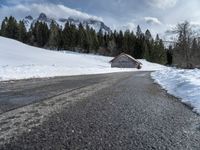 a road that runs to a cabin in the snow with mountains in the background behind