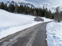 a road that runs to a cabin in the snow with mountains in the background behind