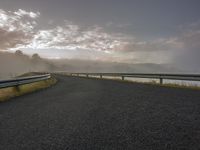 an empty road with a view of the ocean on a foggy day, overlooking