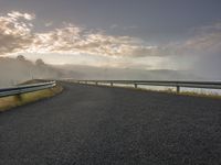 an empty road with a view of the ocean on a foggy day, overlooking