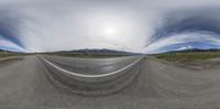 a wide angle image of a road surrounded by mountains and grass in a convex mirror