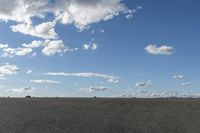 a black car driving in a gravel road next to the ocean on a clear day