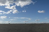 a black car driving in a gravel road next to the ocean on a clear day