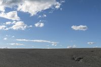 a black car driving in a gravel road next to the ocean on a clear day