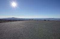 a person is riding a skateboard on a flat surface road with mountains and the sun above them