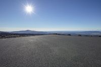 a person is riding a skateboard on a flat surface road with mountains and the sun above them