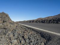 an empty road with rocks and gravel in the foreground, and a large rock wall