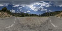 a two way street going into the mountains under a cloudy sky and a person standing in the middle