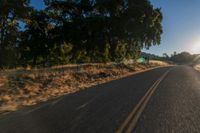 an asphalt road in the evening with the sun setting over it and trees behind it