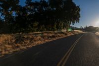 an asphalt road in the evening with the sun setting over it and trees behind it