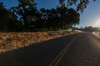 an asphalt road in the evening with the sun setting over it and trees behind it