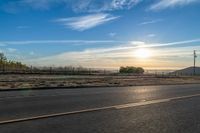 the sun rises over a small mountain on a highway that goes into the distance as a horse is standing in the foreground